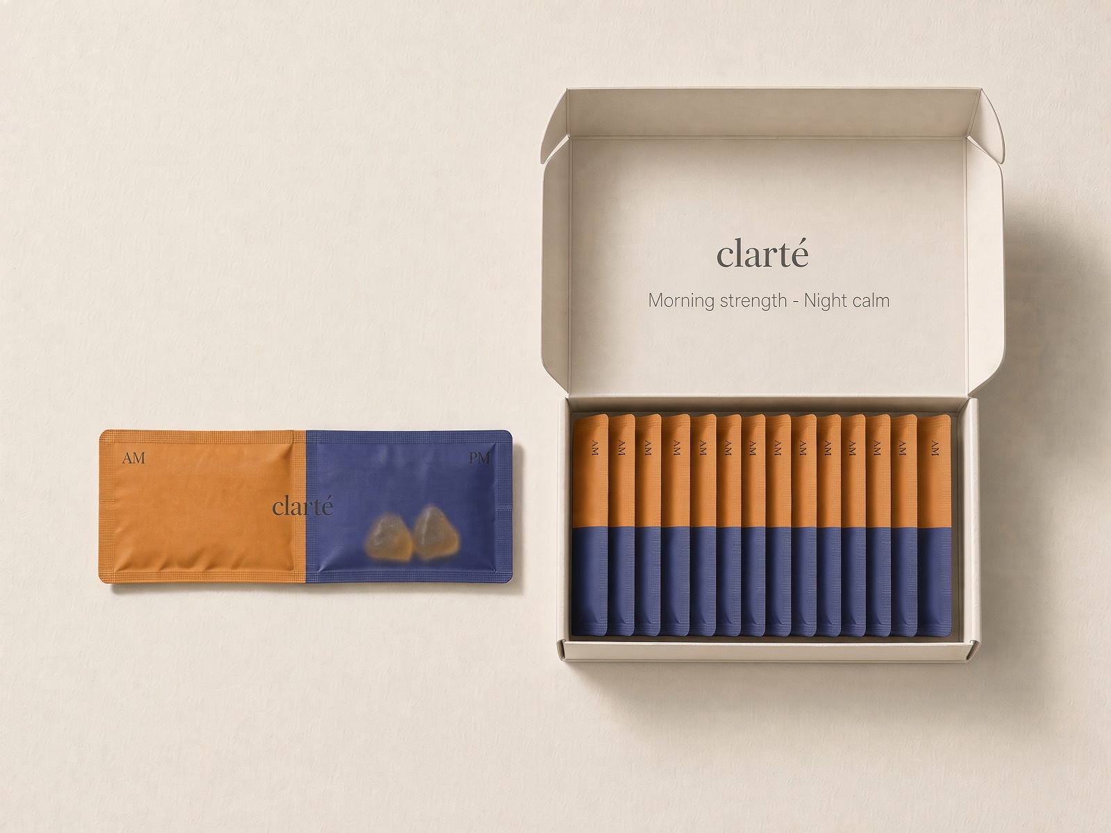 An open Clarté box holding a row of AM/PM sachets, with one sachet beside it: an amber morning half for the creatine and an indigo evening half holding two magnesium gummies.